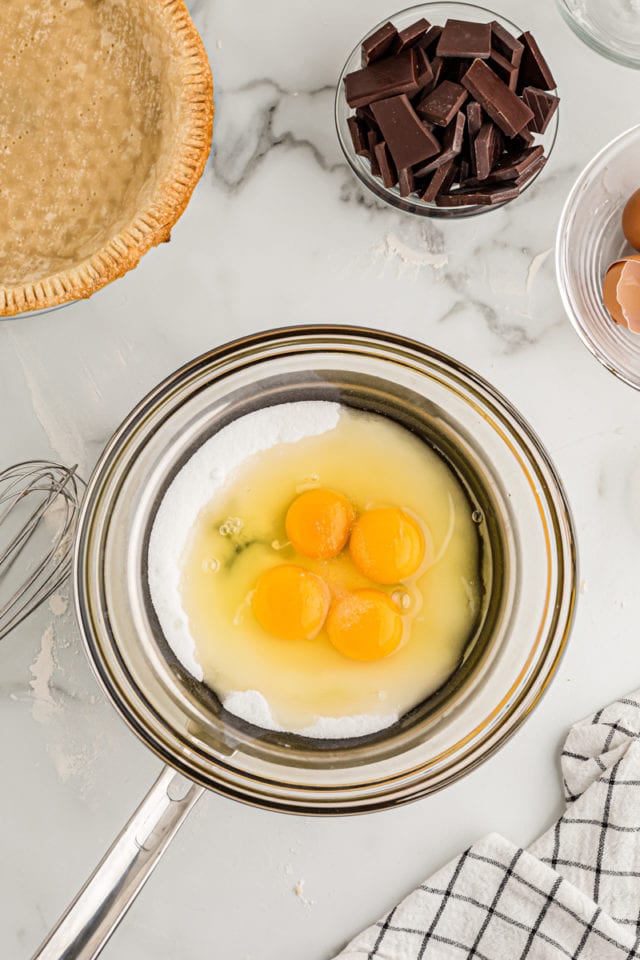 Overhead view of eggs and sugar in glass bowl over saucepan