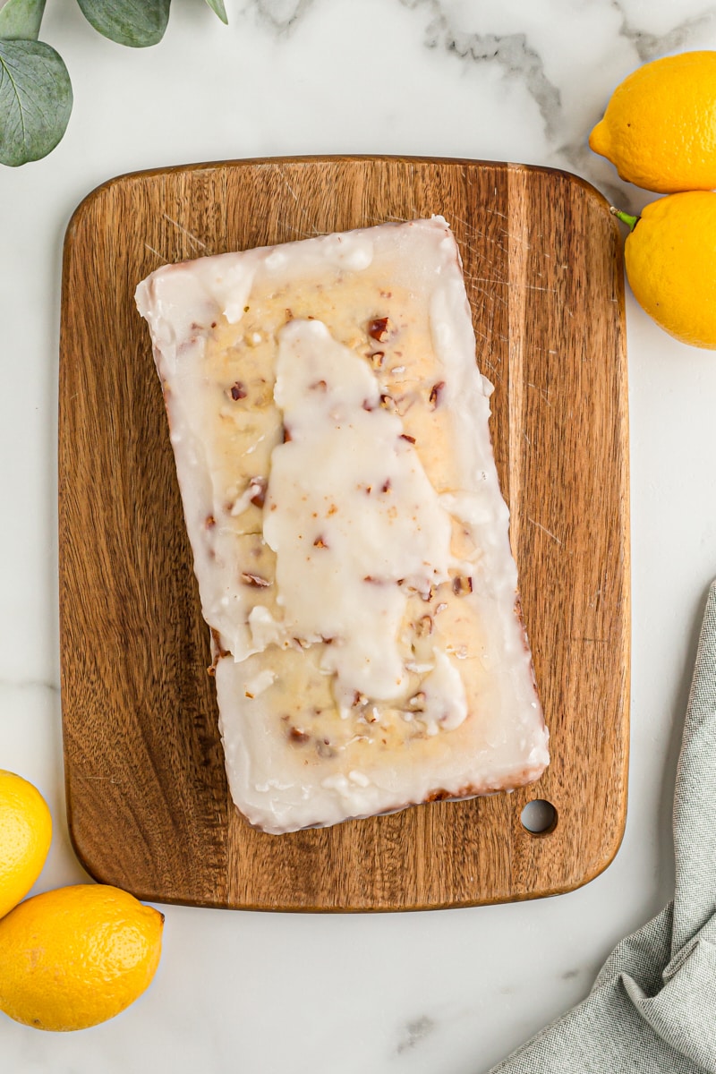 Overhead view of glazed lemon bread on wood board with lemons