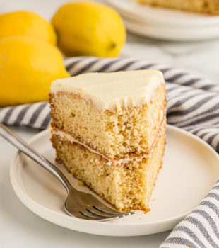 Slice of lemon cream cake on plate, with bite taken out of tip
