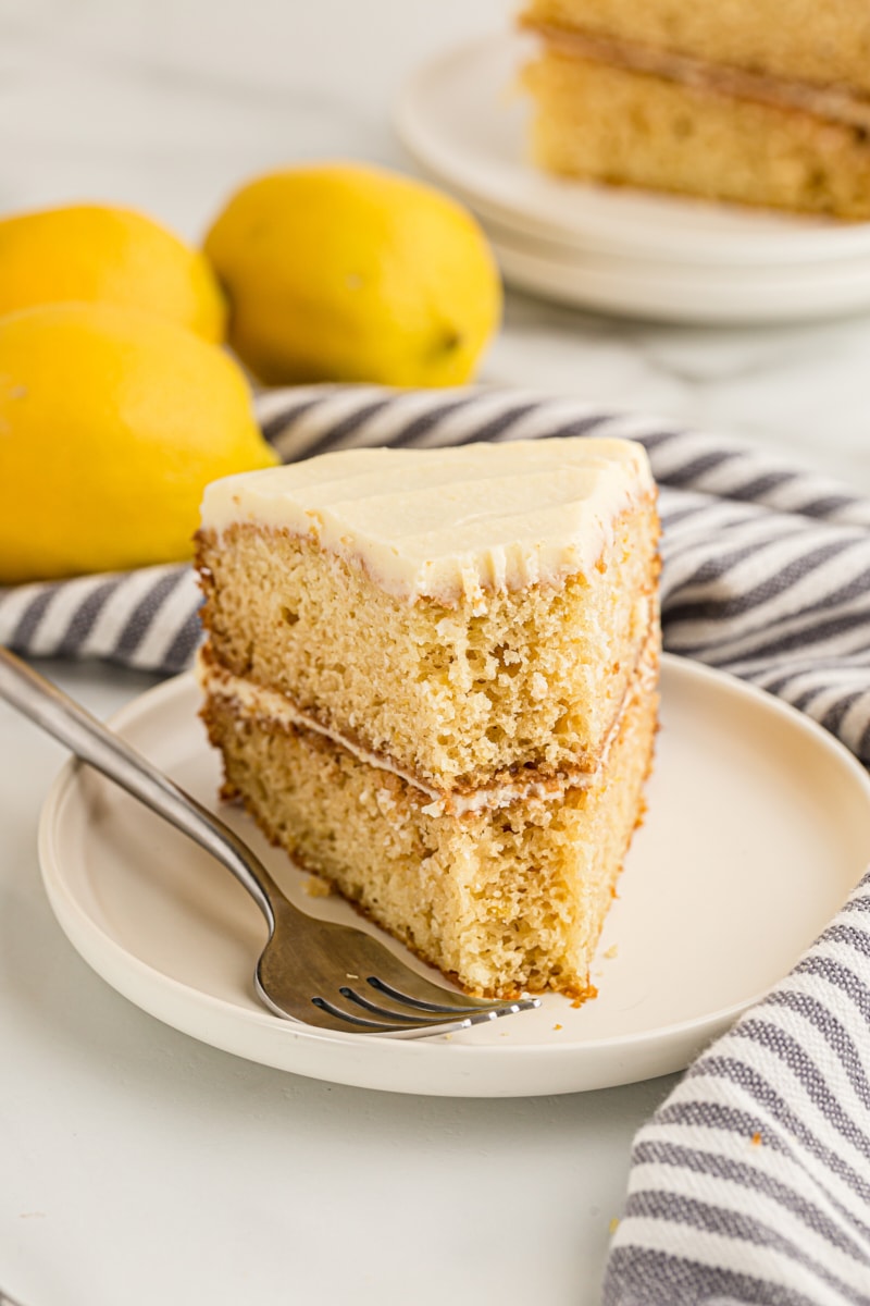 Slice of lemon cream cake on plate, with bite taken out of tip