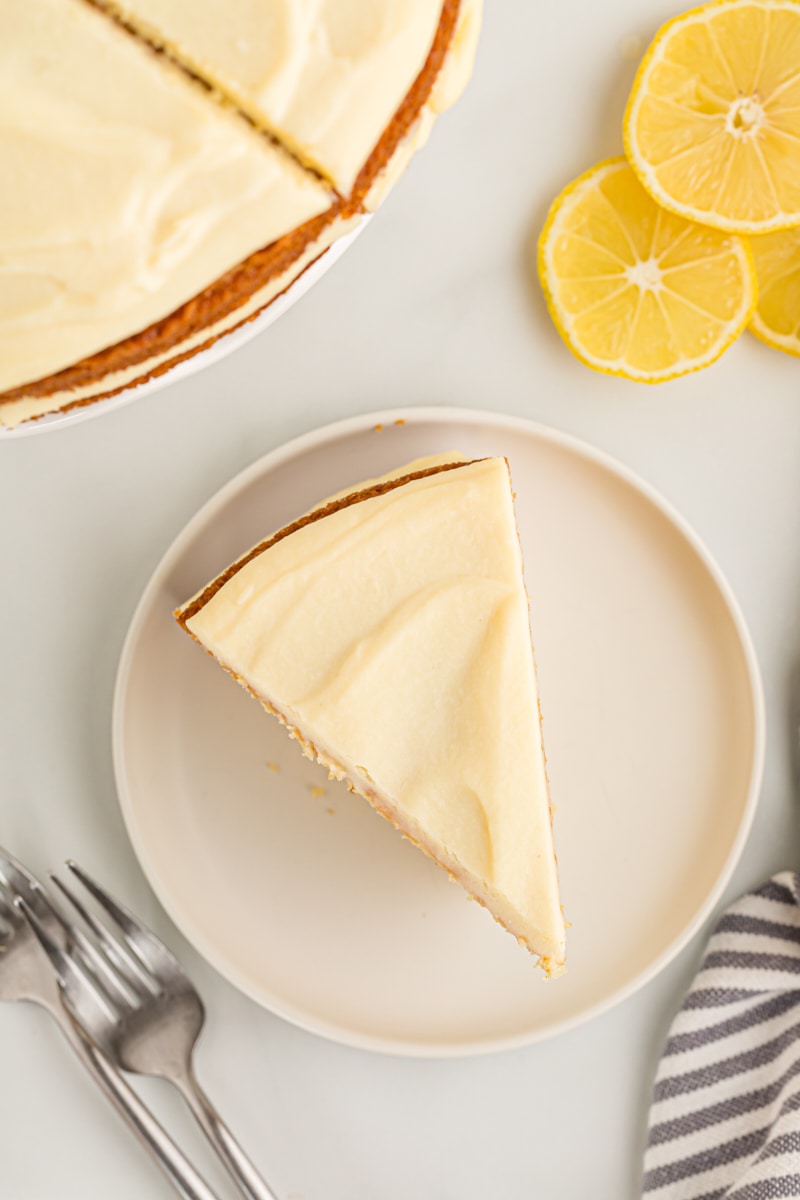 Overhead view of lemon cream cake slice on plate, with remaining cake and slices of lemon in background