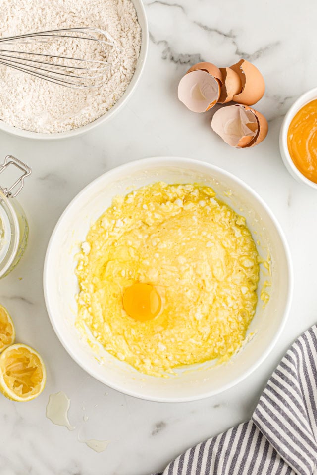 Overhead view of egg added to mixing bowl of lemon cream cake batter