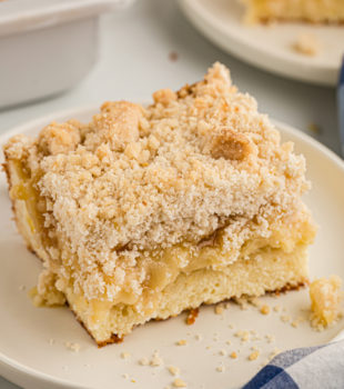 Piece of lemon yogurt crumb cake on plate, with another plate of cake in background