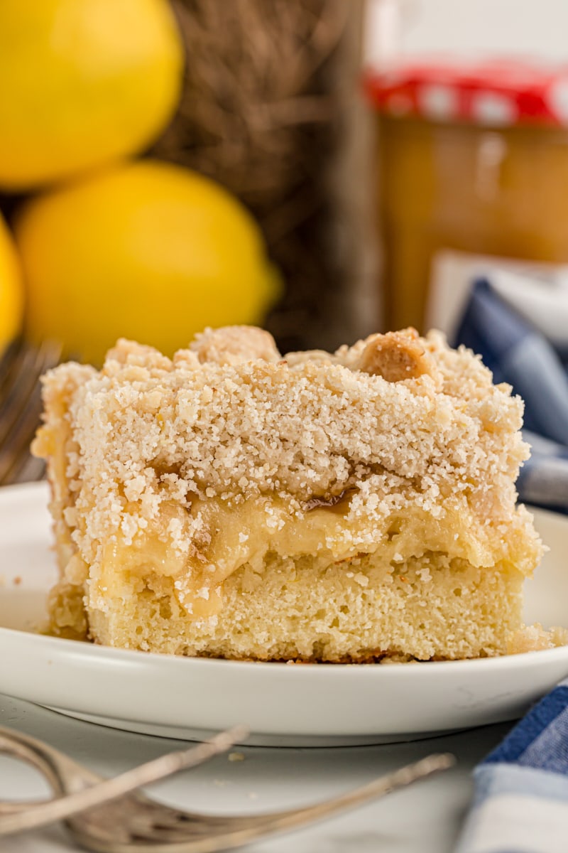 Piece of lemon yogurt crumb cake on plate with lemons in background