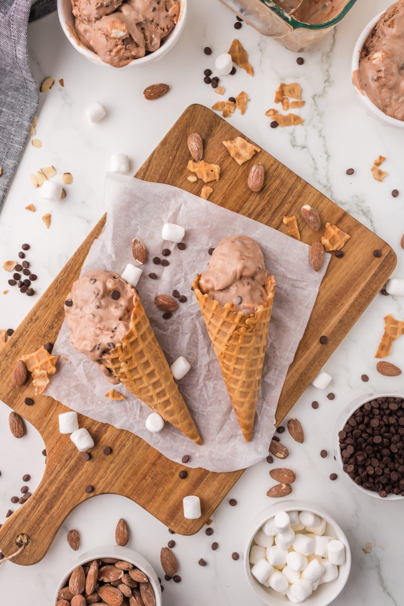 overhead view of rocky road ice cream in waffle cones with chocolate chips, marshmallows, and almonds scattered around