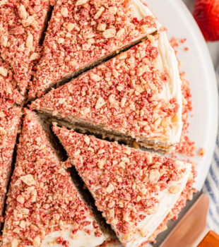 Overhead view of sliced strawberry crunch cake on platter with one slice being removed