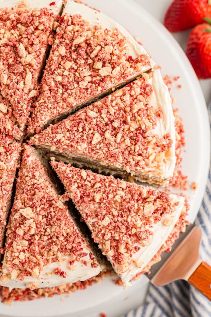 Overhead view of sliced strawberry crunch cake on platter with one slice being removed