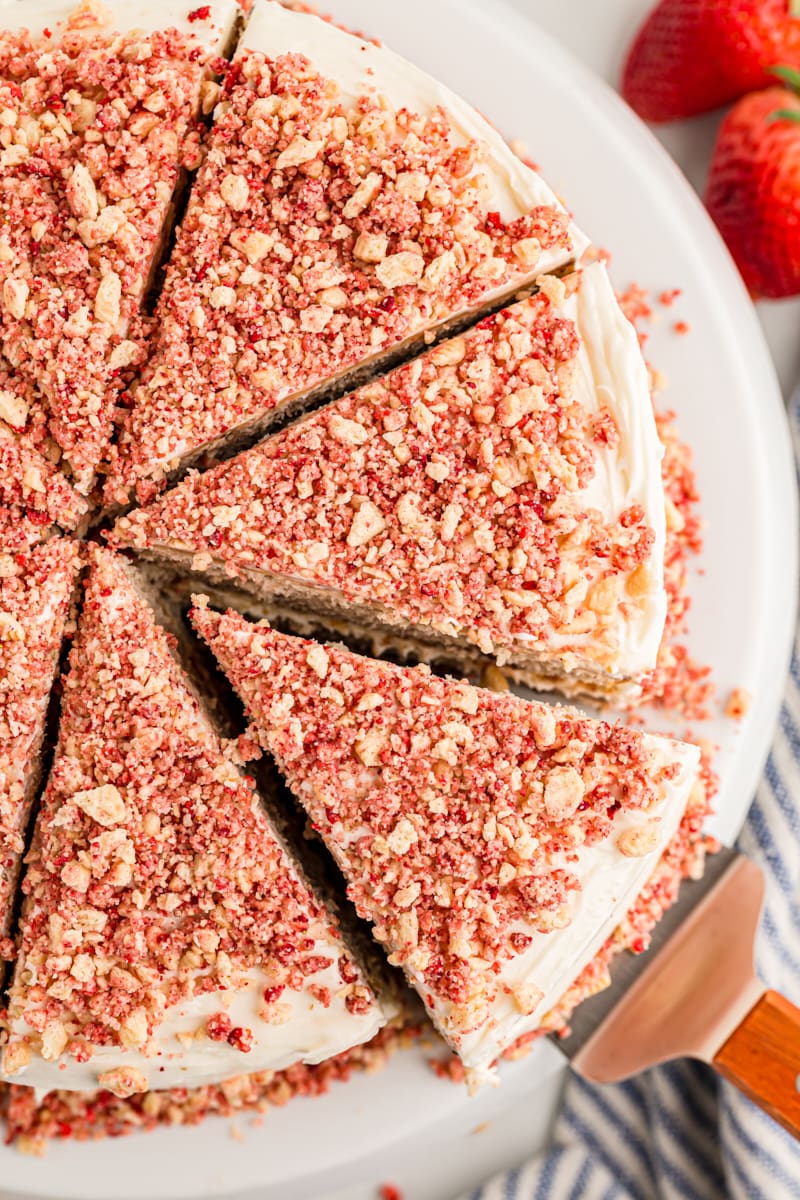 Overhead view of sliced strawberry crunch cake on platter with one slice being removed