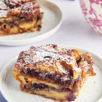Two plates of blueberry croissant bread pudding dusted with powdered sugar