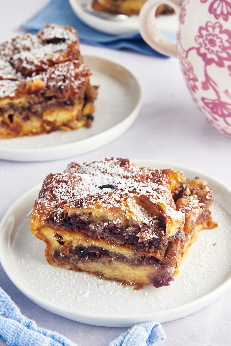 Two plates of blueberry croissant bread pudding dusted with powdered sugar