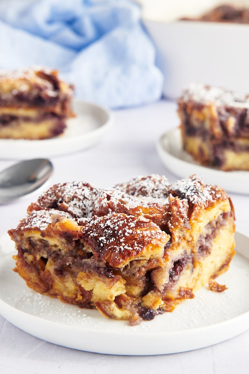 Piece of blueberry croissant bread pudding on plate, topped with powdered sugar