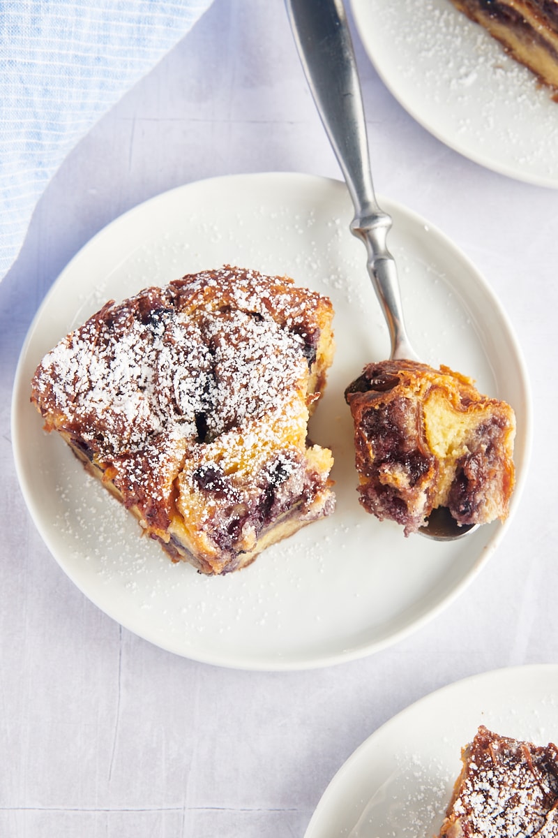 Overhead view of blueberry croissant bread pudding on plate, with bite of pudding on fork