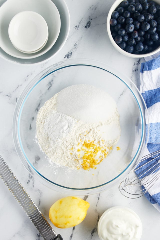 overhead view of flour, sugar, baking powder, baking soda, salt, and lemon zest in a glass mixing bowl