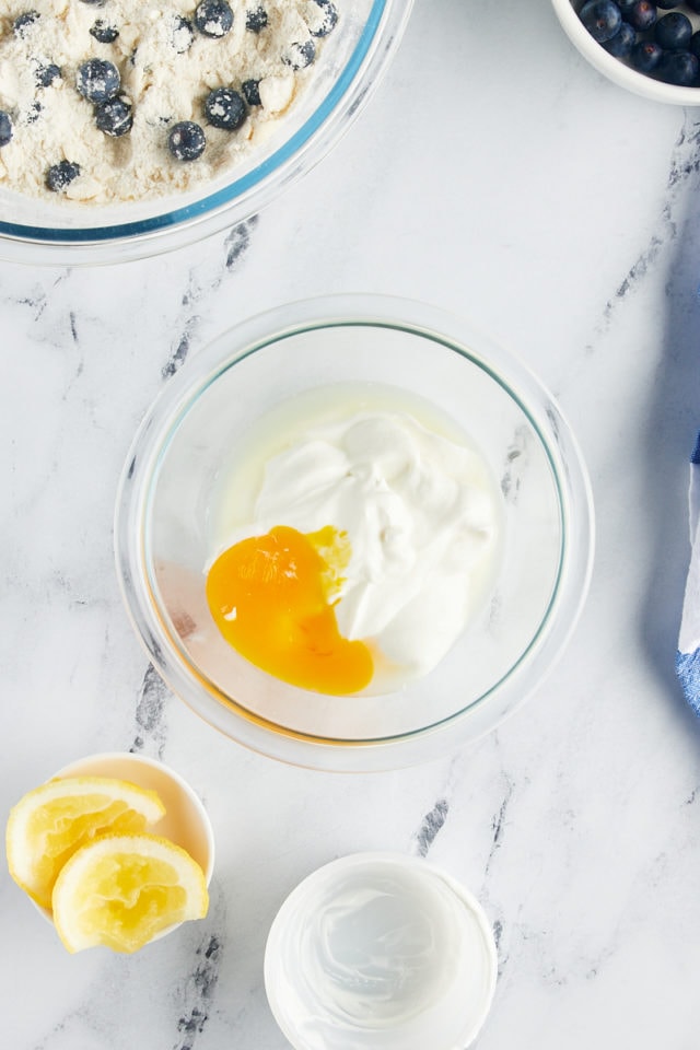 overhead view of Greek yogurt, an egg yolk, and lemon juice in a glass mixing bowl