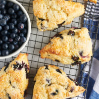 overhead view of blueberry scones and a bowl of blueberries on a wire cooling rack