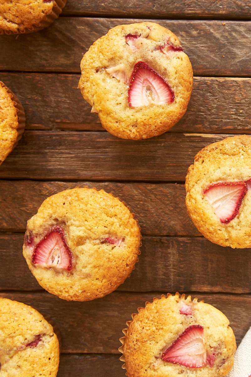 overhead view of strawberry muffins scattered on a wooden surface