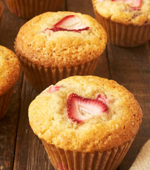 a strawberry muffin on a wooden surface with more muffins in the background