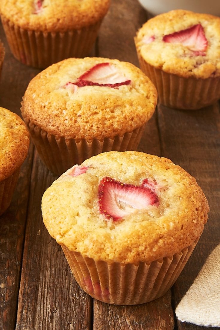 a strawberry muffin on a wooden surface with more muffins in the background
