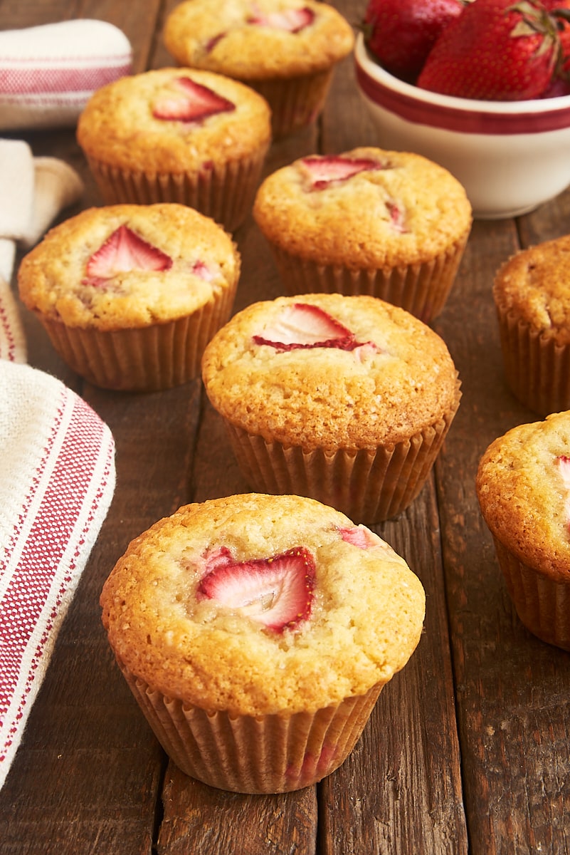 strawberry muffins and a bowl of strawberries on a wooden surface