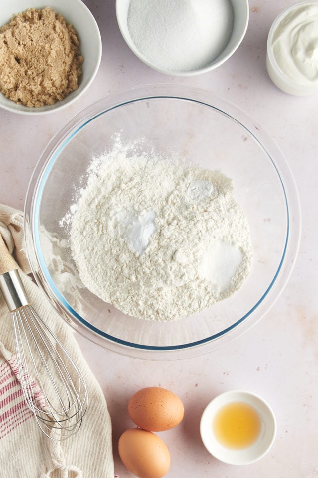 overhead view of flour, baking powder, baking soda, and salt in a glass mixing bowl