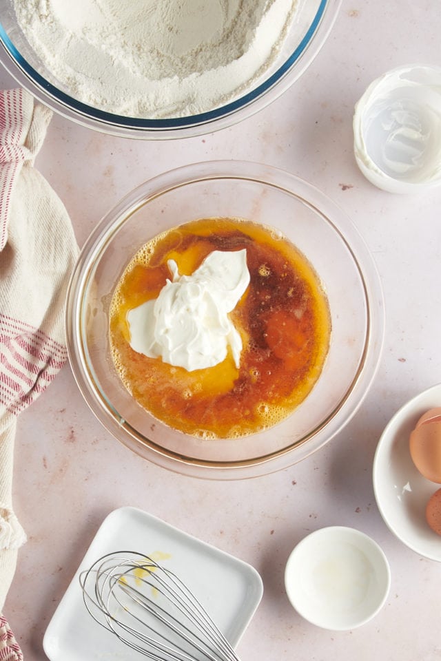 overhead view of eggs, brown butter, sour cream, and vanilla extract in a glass mixing bowl