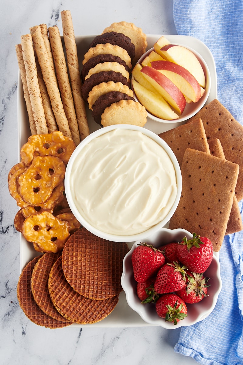 Overhead view of cheesecake dip in bowl on tray with crackers, cookies, and fruit