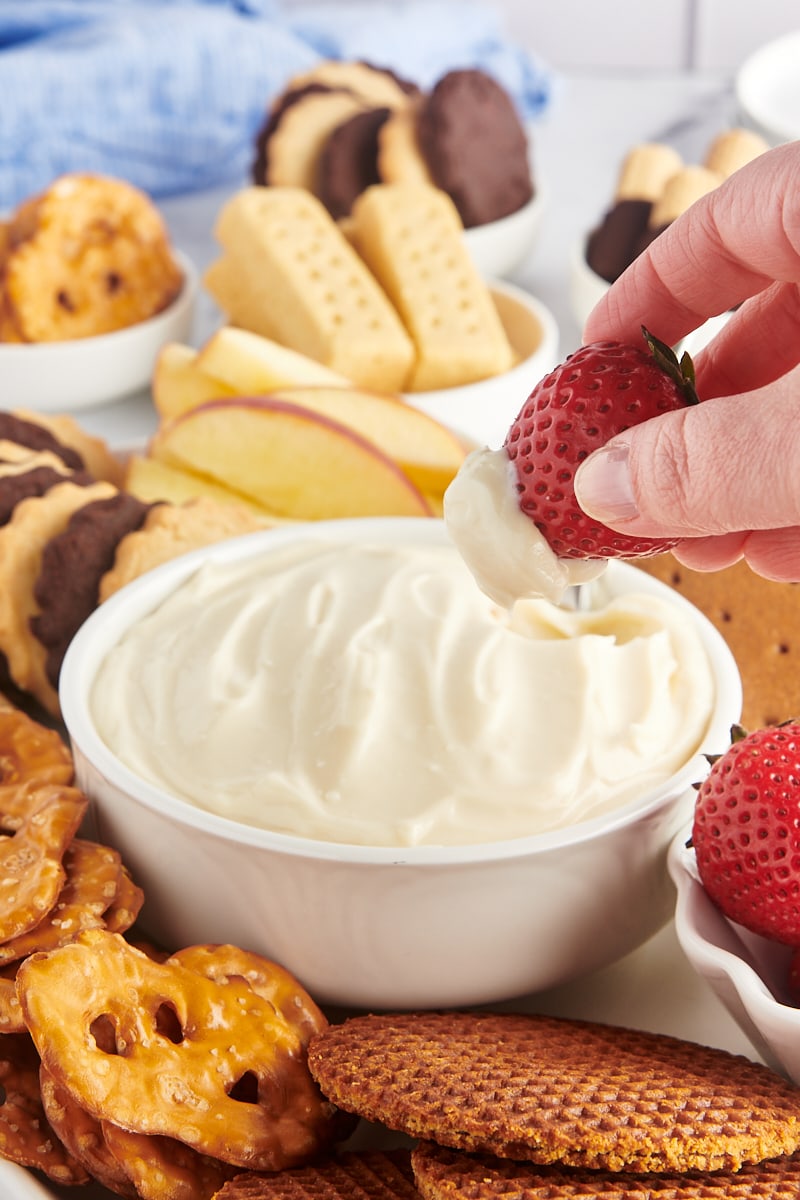 Hand dipping a strawberry into a bowl of cheesecake dip