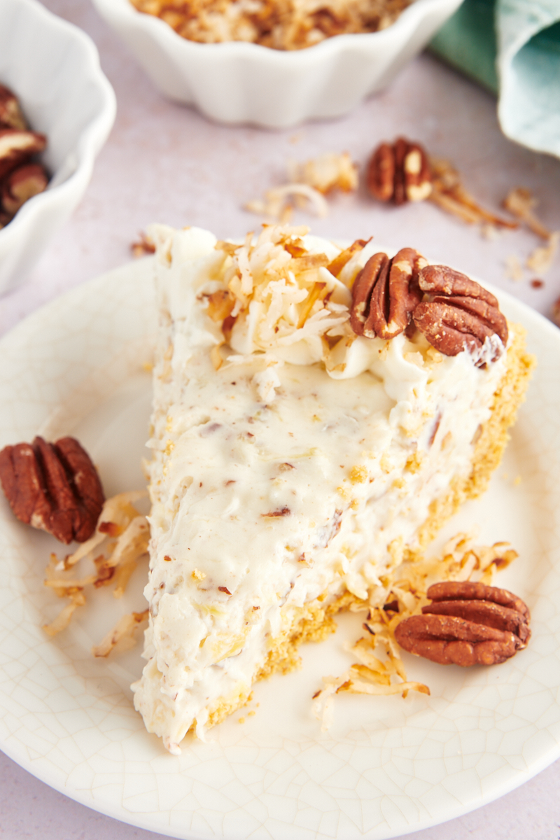 Millionaire pie is a no-bake dessert that combines crushed pineapple, pecans, and coconut with a fluffy whipped filling. Perfect for summer! Slice of millionaire pie on plate with toasted coconut and pecans for garnish