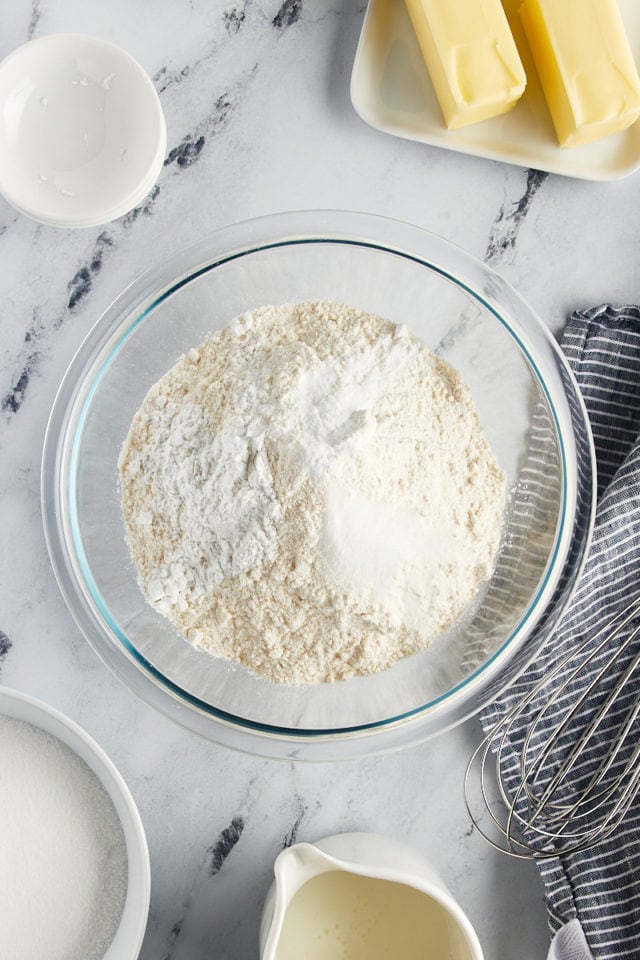 overhead view of flour, baking powder, baking soda, and salt in a glass mixing bowl