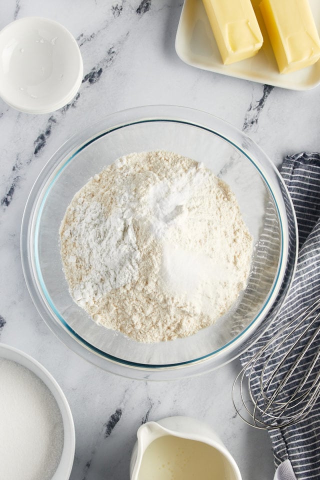 Overhead view of flour, baking powder, baking soda, and salt in a glass mixing bowl.