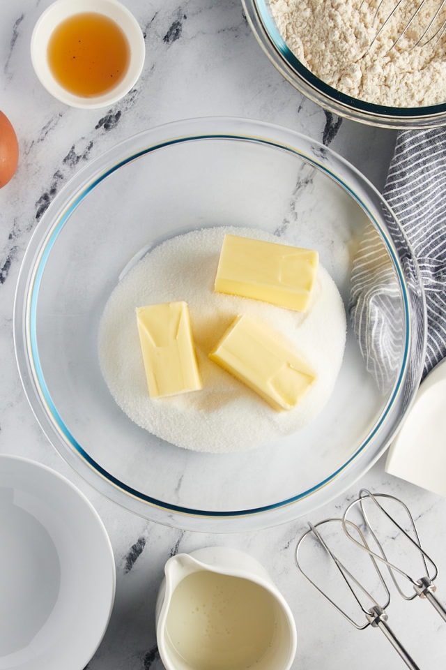 Overhead view of butter and sugar in a glass mixing bowl.