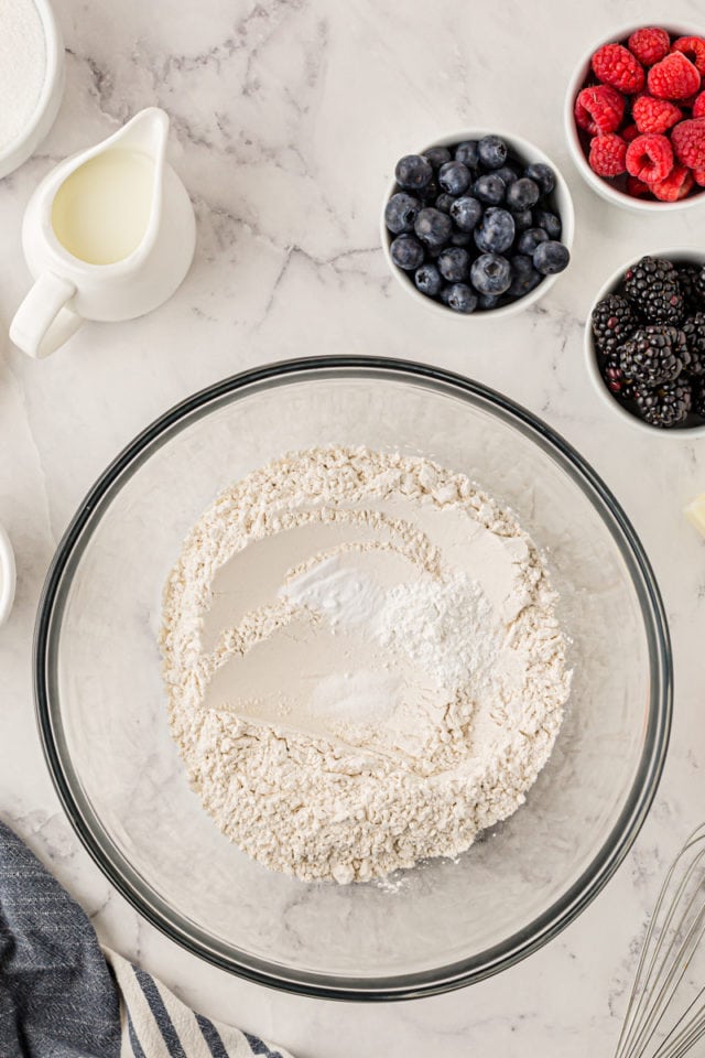 overhead view of flour, baking powder, baking soda, and salt in a glass mixing bowl