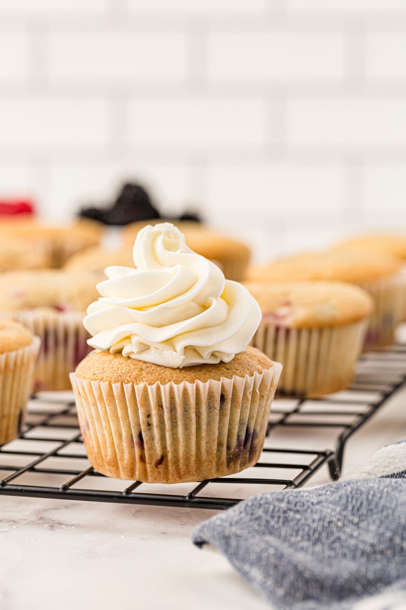 a frosted berry cupcake on a wire rack surrounded by more cupcakes