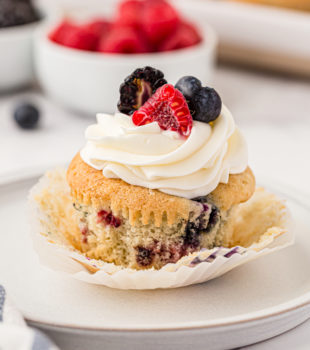 a berry cupcake on a white plate with berries and more cupcakes in the background