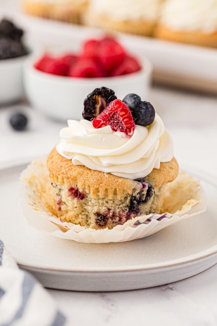 a berry cupcake on a white plate with berries and more cupcakes in the background