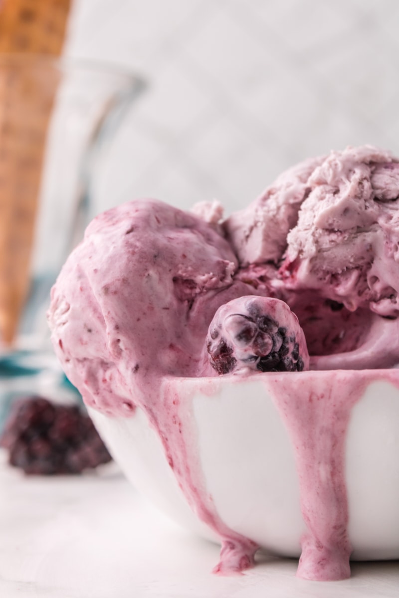 a bowl of blackberry ice cream with some melting over the side of the bowl