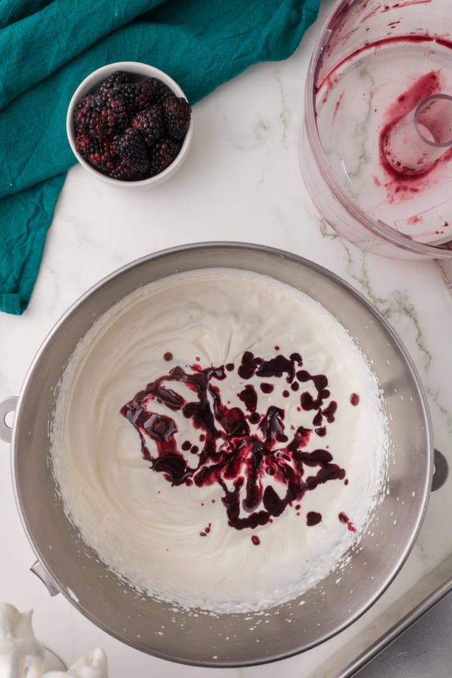 overhead view of raspberry puree added to lightly whipped cream in a metal mixing bowl