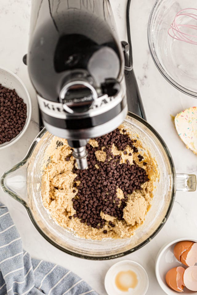 overhead view of chocolate chips added to cookie dough in the bowl of a stand mixer