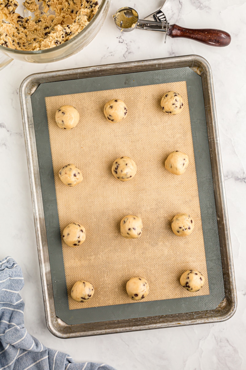 overhead view of portioned chocolate chip cookie dough on a baking sheet lined with a silicone liner