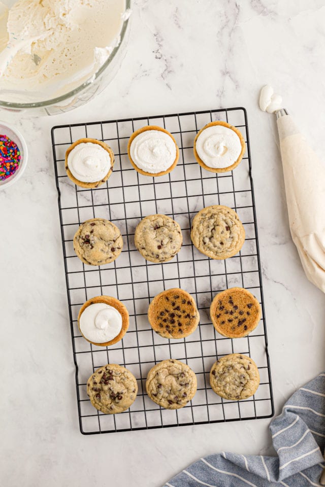 overhead view of chocolate chip cookies on a wire rack, with frosting piped onto the bottoms of some of the cookies