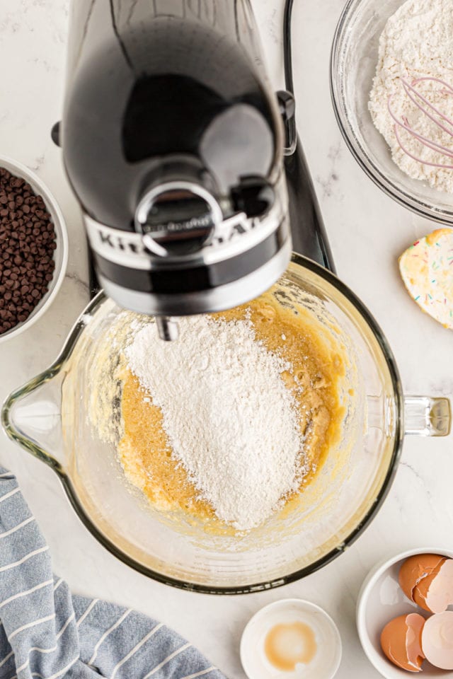 overhead view of flour added to cookie dough in the bowl of a stand mixer