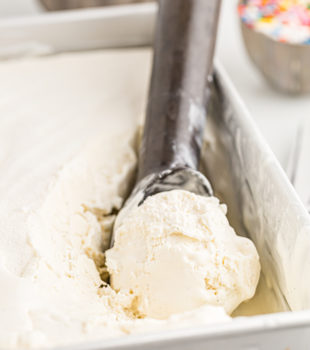 Scoop of vanilla ice cream in ice cream scooper, set inside loaf pan