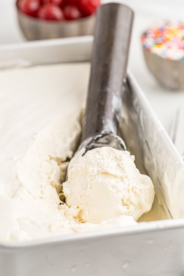 Scoop of vanilla ice cream in ice cream scooper, set inside loaf pan