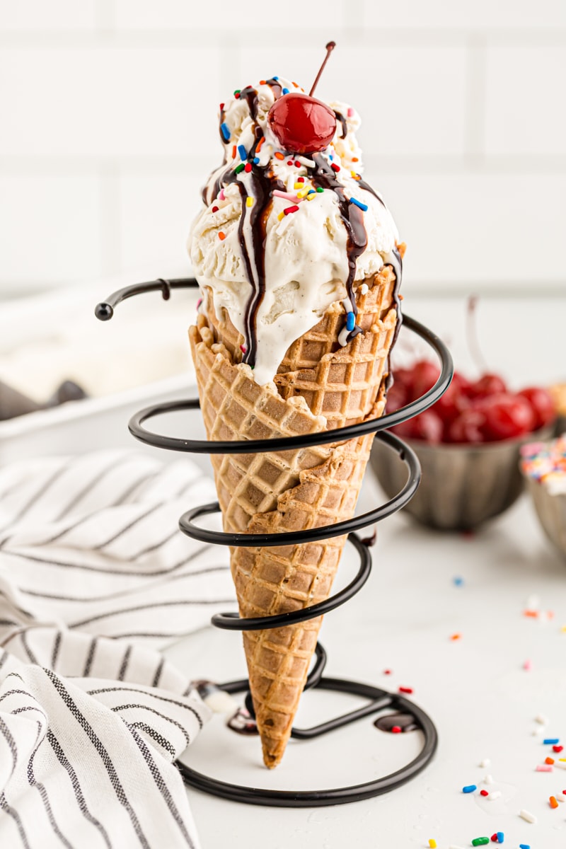 Waffle cone with vanilla ice cream, sprinkles, chocolate sauce, and cherry
