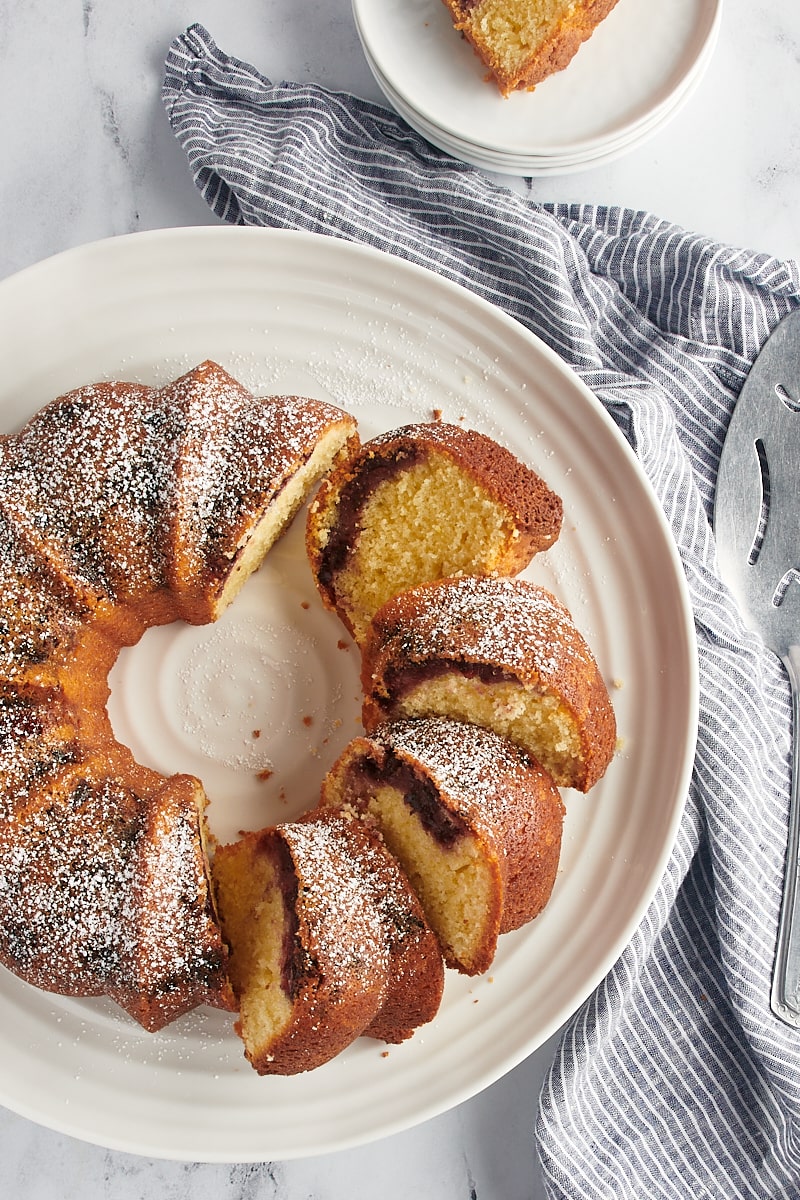 overhead view of black cherry sour cream coffee cake partially sliced on a cake stand