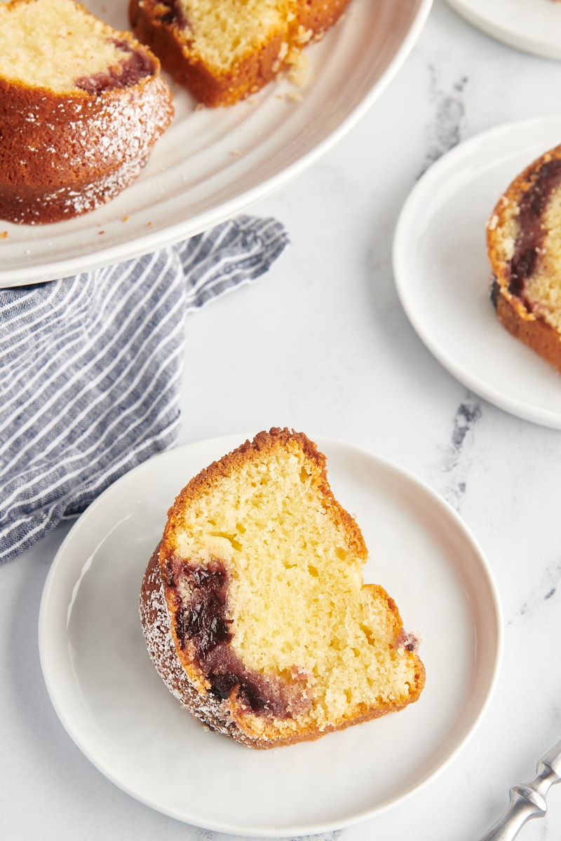 a slice of black cherry sour cream coffee cake on a white plate with remaining cake behind