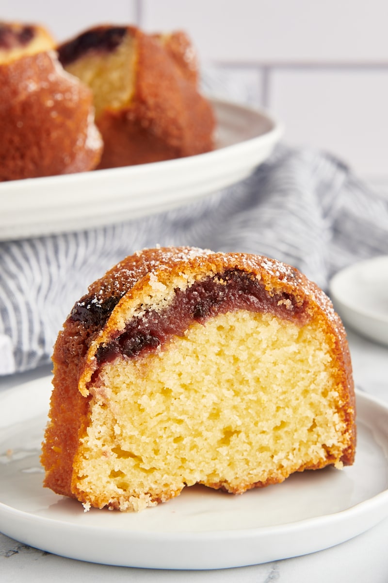 slice of black cherry sour cream coffee cake on a white plate with remaining cake in the background