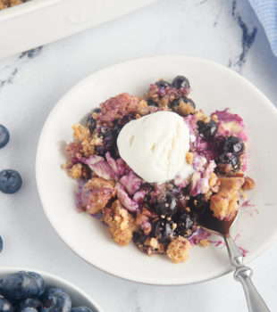 Blueberry crisp on white plate with scoop of vanilla ice cream and spoon