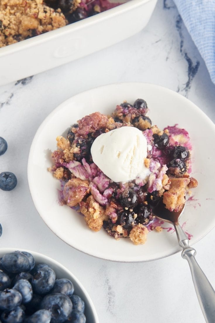 Blueberry crisp on white plate with scoop of vanilla ice cream and spoon
