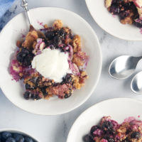 Overhead view of blueberry crisp on 3 white plates, center with scoop of vanilla ice cream